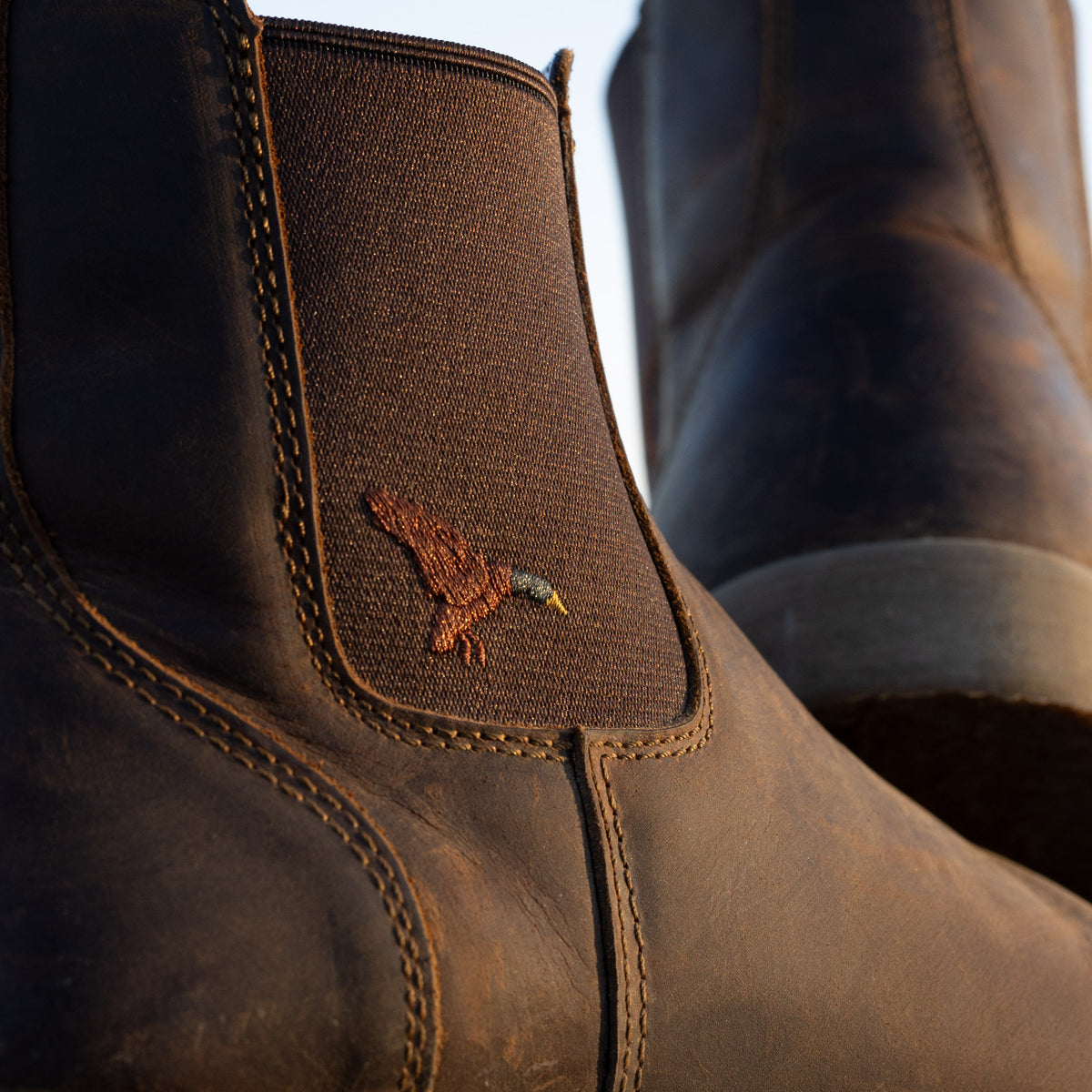 Close-up of Dive Bomb Dark Walnut Heritage Boot with a brown fabric ankle patch featuring an embroidered mallard logo.