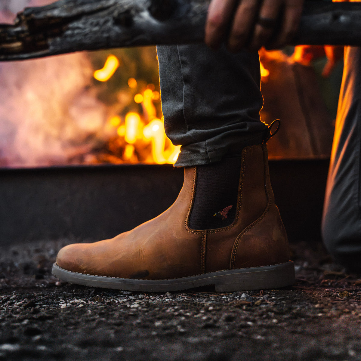 Dive Bomb Tobacco Brown Heritage Boot in front of a campfire, has a full-grain cowhide upper.